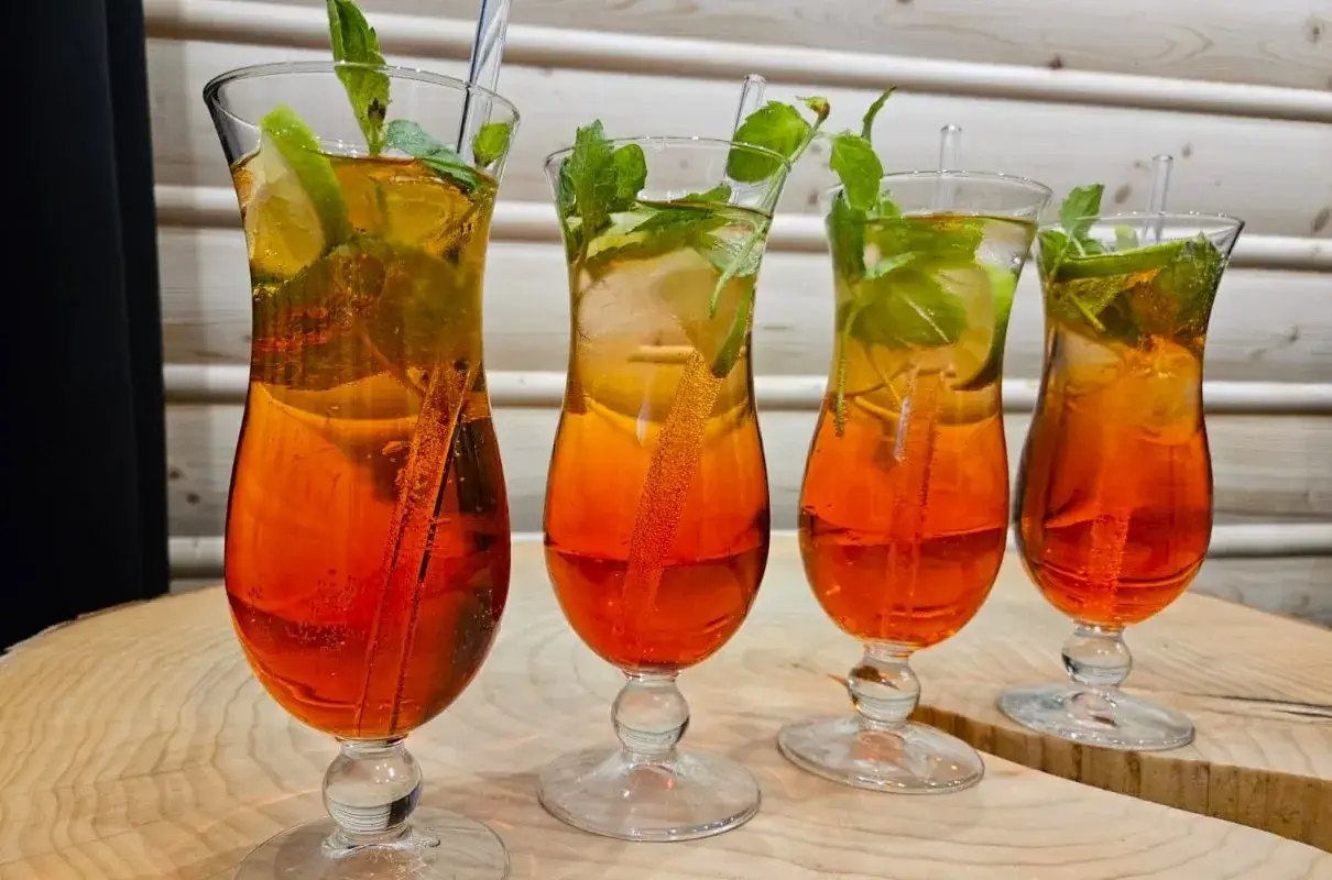 Orzeźwiający pomarańczowy mocktail z lodem, limonką i miętą, podany w eleganckich kieliszkach. Idealny na letnie popołudnie.