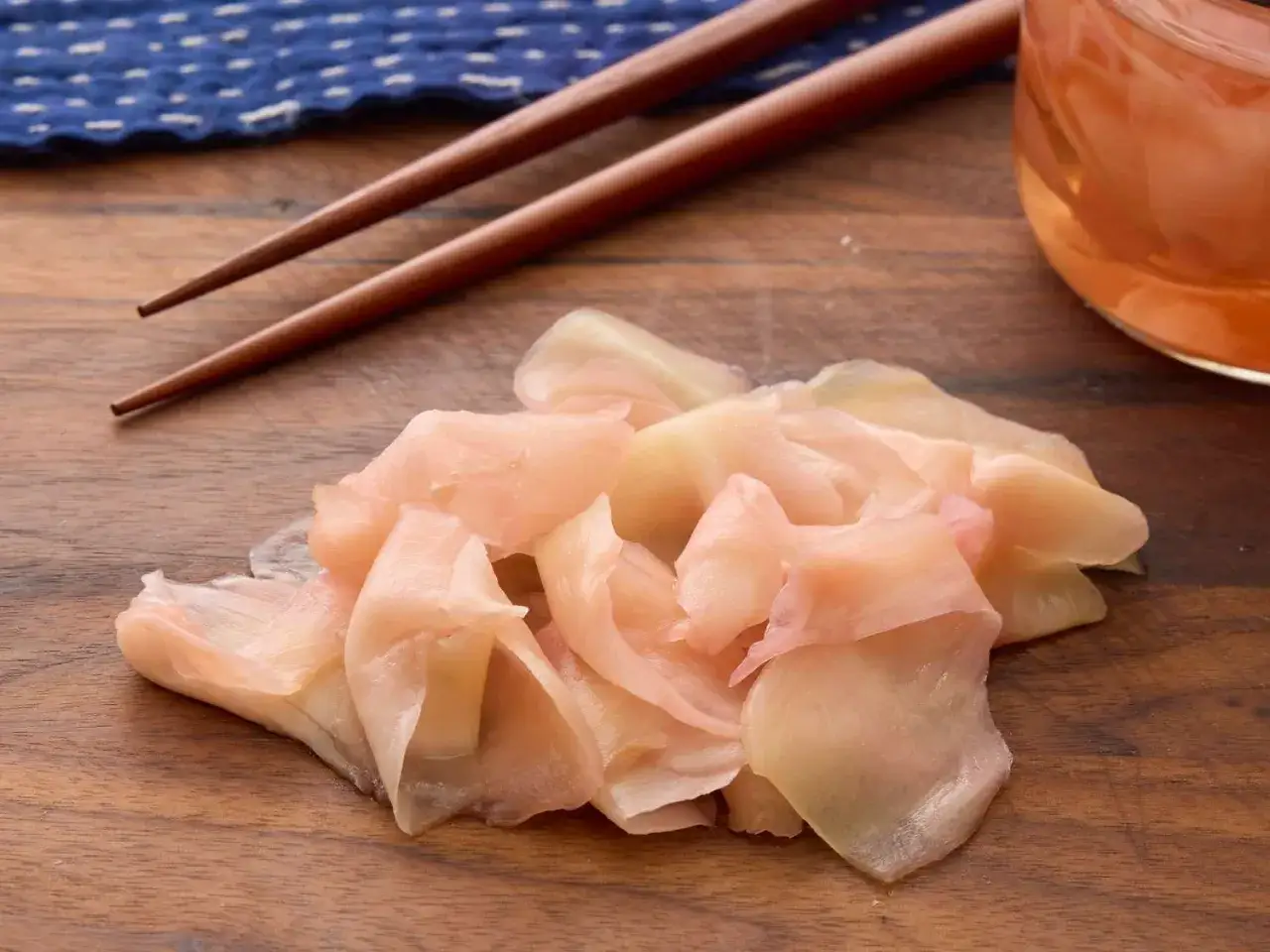 Delikatny, różowy imbir marynowany na drewnianej desce, obok pałeczek i słoiczka z marynatą. Idealny dodatek do sushi.