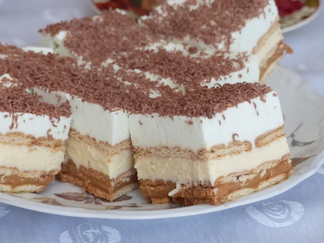 Szybkie ciasto bez pieczenia z budyniem i herbatnikami, udekorowane wiórkami czekoladowymi. Idealne na deser!