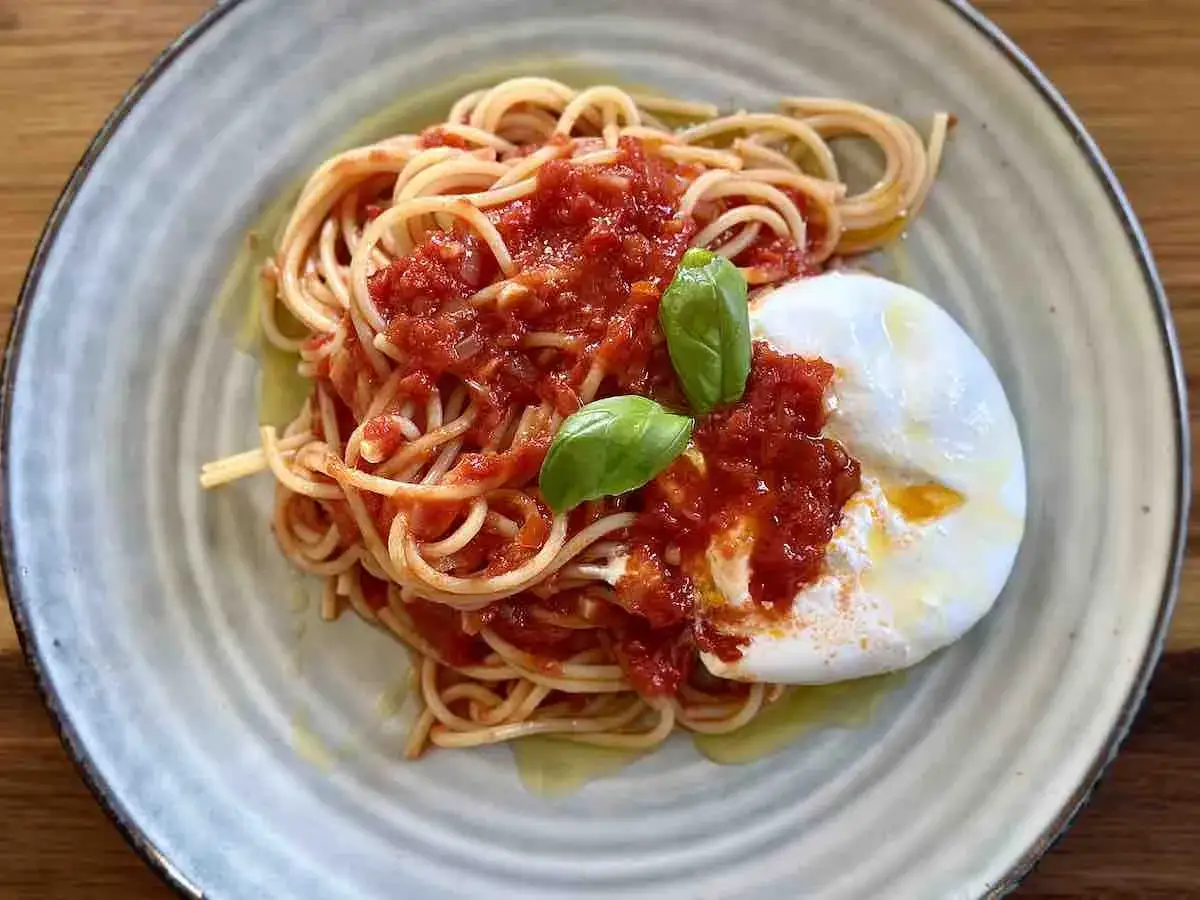 Spaghetti z bogatym sosem do makaronu, polane oliwą, z kremową burratą i listkami bazylii. Pyszne danie.