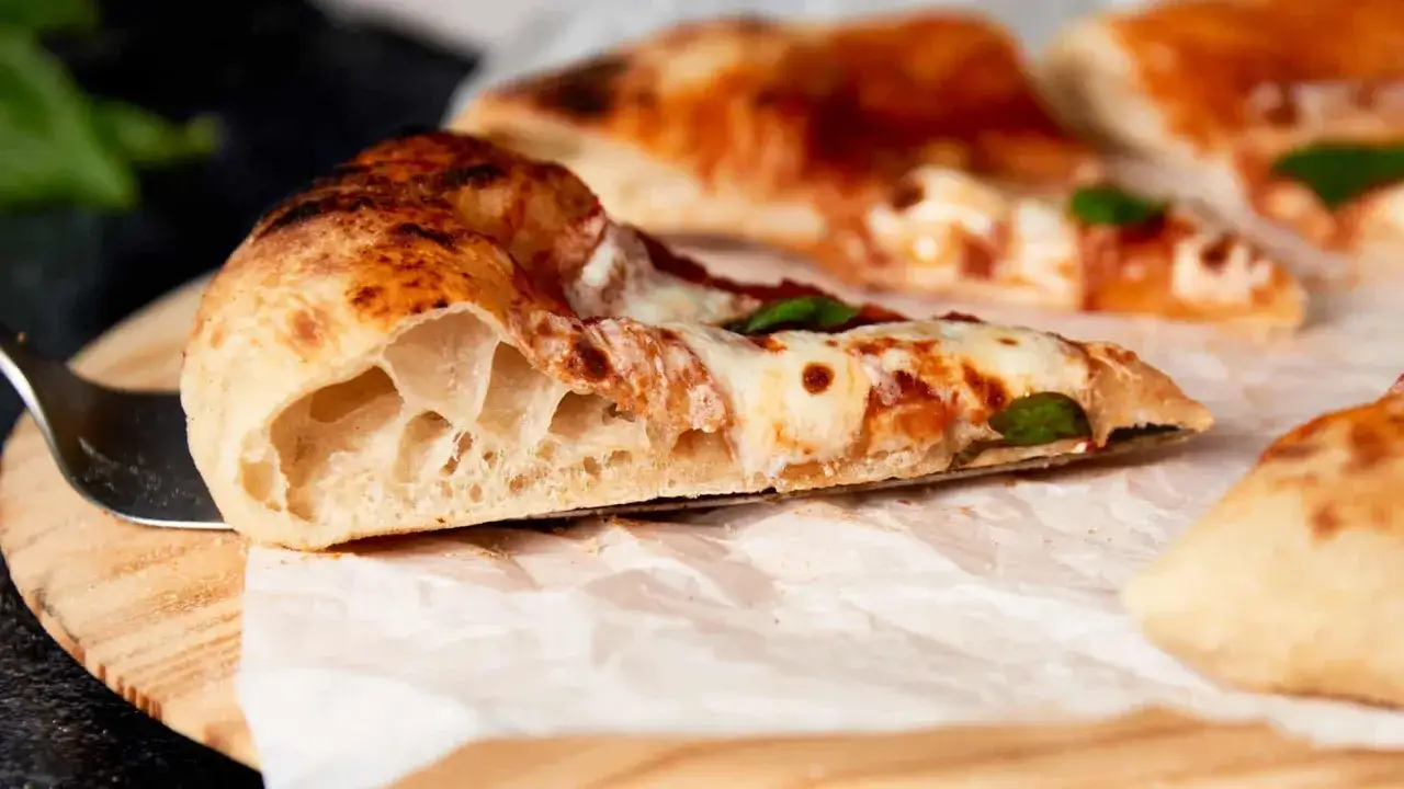Puszyste, lekko przypieczone ciasto na pizzę neapolitańską z widocznymi pęcherzykami powietrza, pokryte sosem pomidorowym i mozzarellą.
