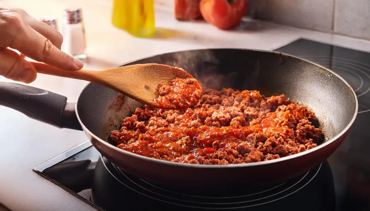 Mieszanie mielonego mięsa z sosem pomidorowym na patelni, by dowiedzieć się, jak doprawić mięso mielone do spaghetti.