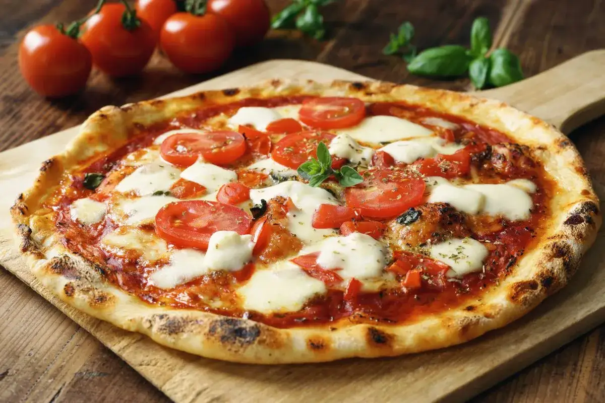 Pyszna pizza capriciosa z pomidorami i mozzarellą, ozdobiona świeżą bazylią, na drewnianej desce.