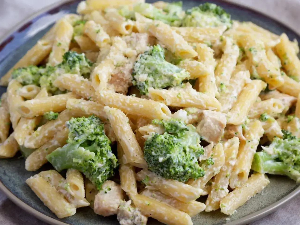 Penne z kurczakiem i brokułami w kremowym sosie, posypane parmezanem. Pyszne danie obiadowe.