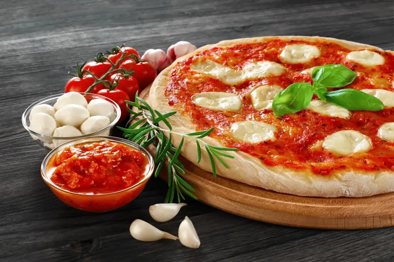 Klasyczna margarita pizza z pomidorami, mozzarellą i bazylią. Obok składniki: pomidorki, kulki mozzarelli, sos pomidorowy, czosnek i rozmaryn.