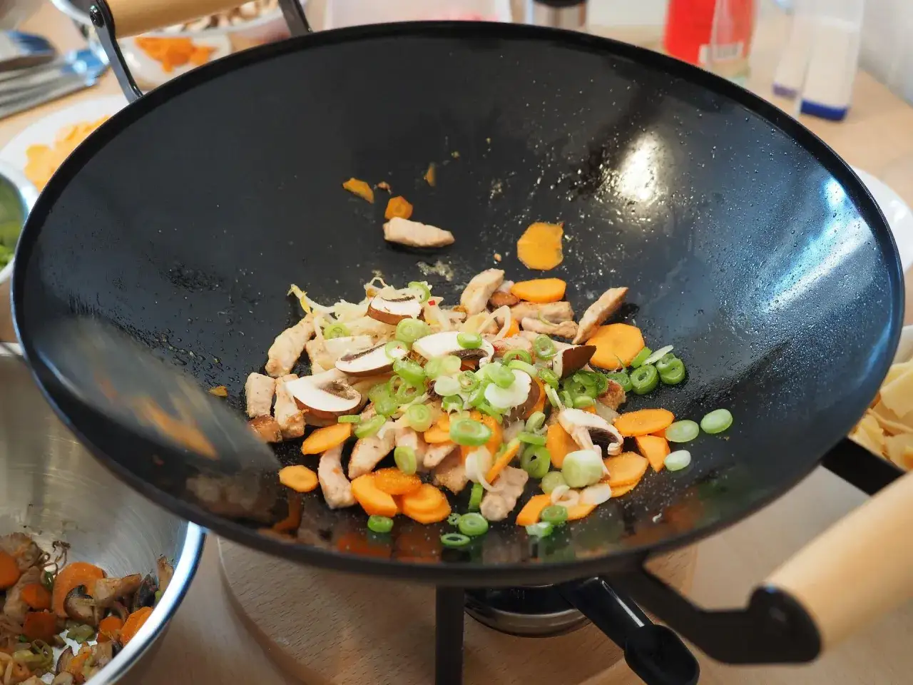 Na patelni wok smaży się pyszny stir fry z kurczakiem, marchewką, pieczarkami i szczypiorkiem.