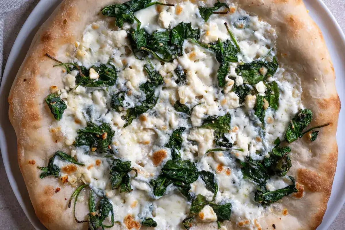 Pyszna pizza ze szpinakiem i białym serem, z chrupiącym, złocistym brzegiem.