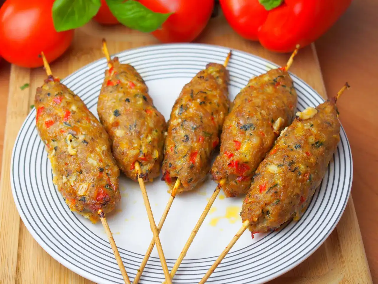 Pięć soczystych kebabów z mięsa mielonego, przyprawionych i podanych na talerzu z warzywami w tle.