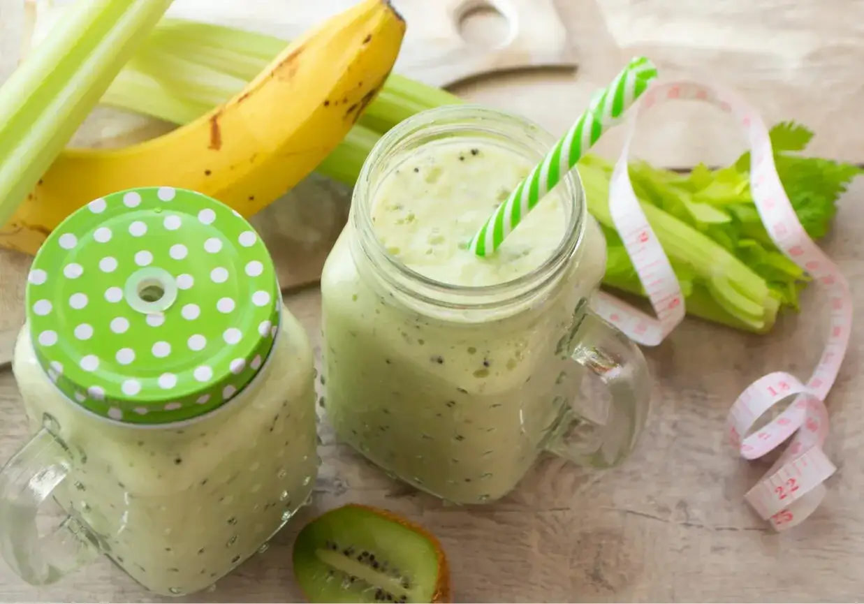 Zielony koktajl z pietruszki i banana, idealny na zdrowy początek dnia. Obok leżą świeże łodygi selera i miarka.