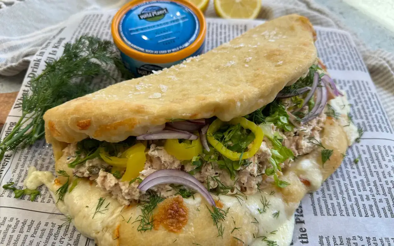 Pyszna pizza z tuńczykiem, sałatą, cebulą i papryką, podana na gazecie.