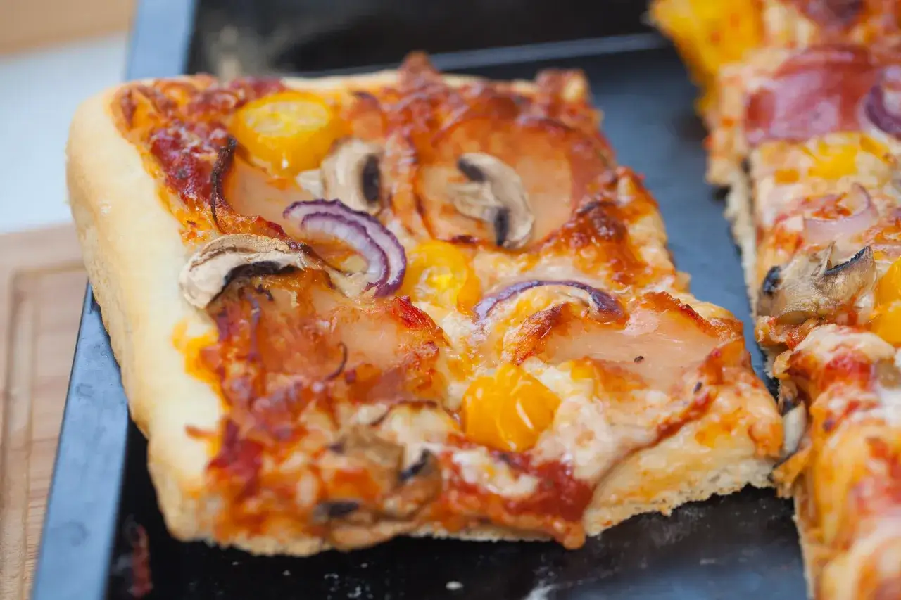 Domowa pizza na blachę, pachnąca świeżymi drożdżami, z pieczarkami, cebulą i żółtymi pomidorkami. Idealna na rodzinny obiad.