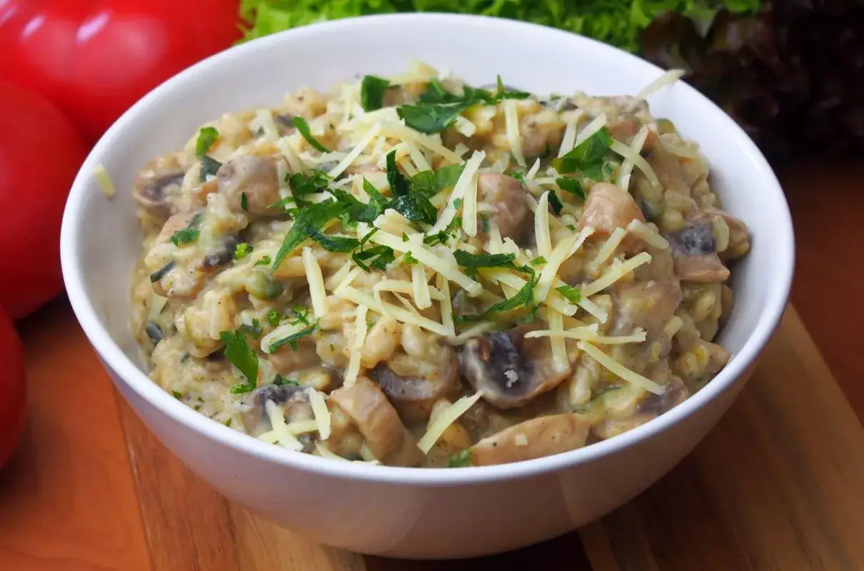 Aksamitne risotto z pieczarkami, posypane startym parmezanem i świeżą natką pietruszki, prezentuje się apetycznie w białej miseczce.