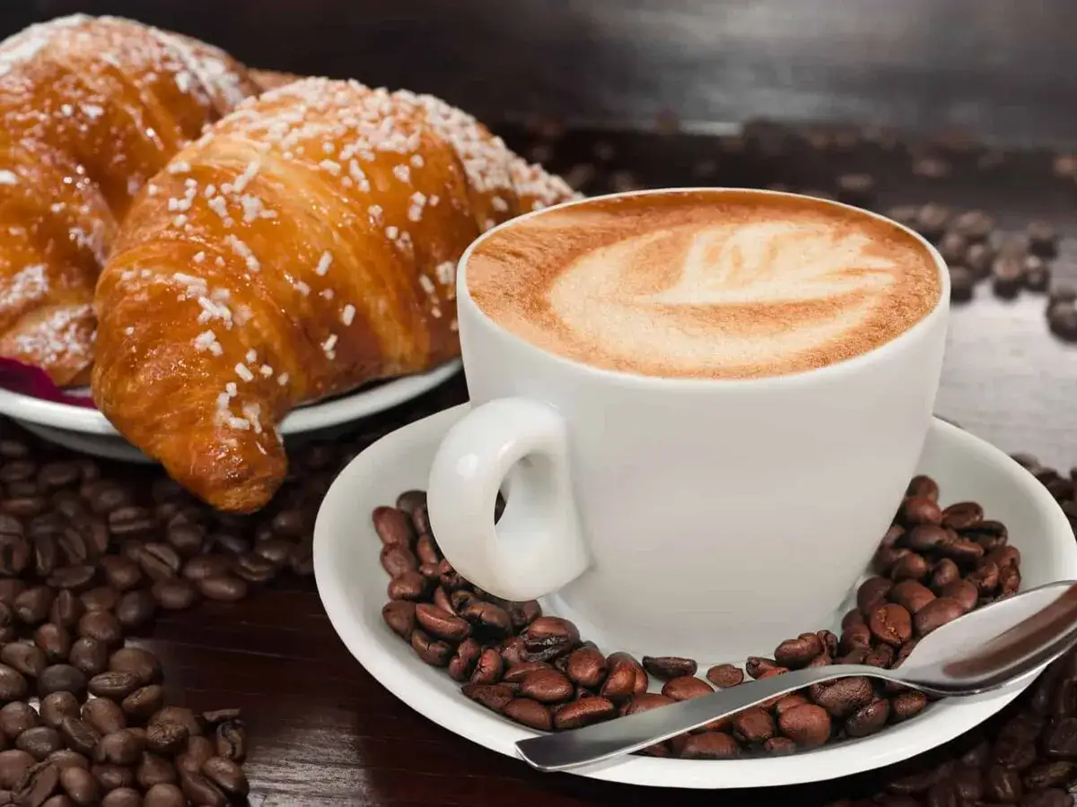Aromaticzne cafe au lait z pianką w kształcie liścia, obok dwa chrupiące rogaliki posypane cukrem i ziarna kawy.