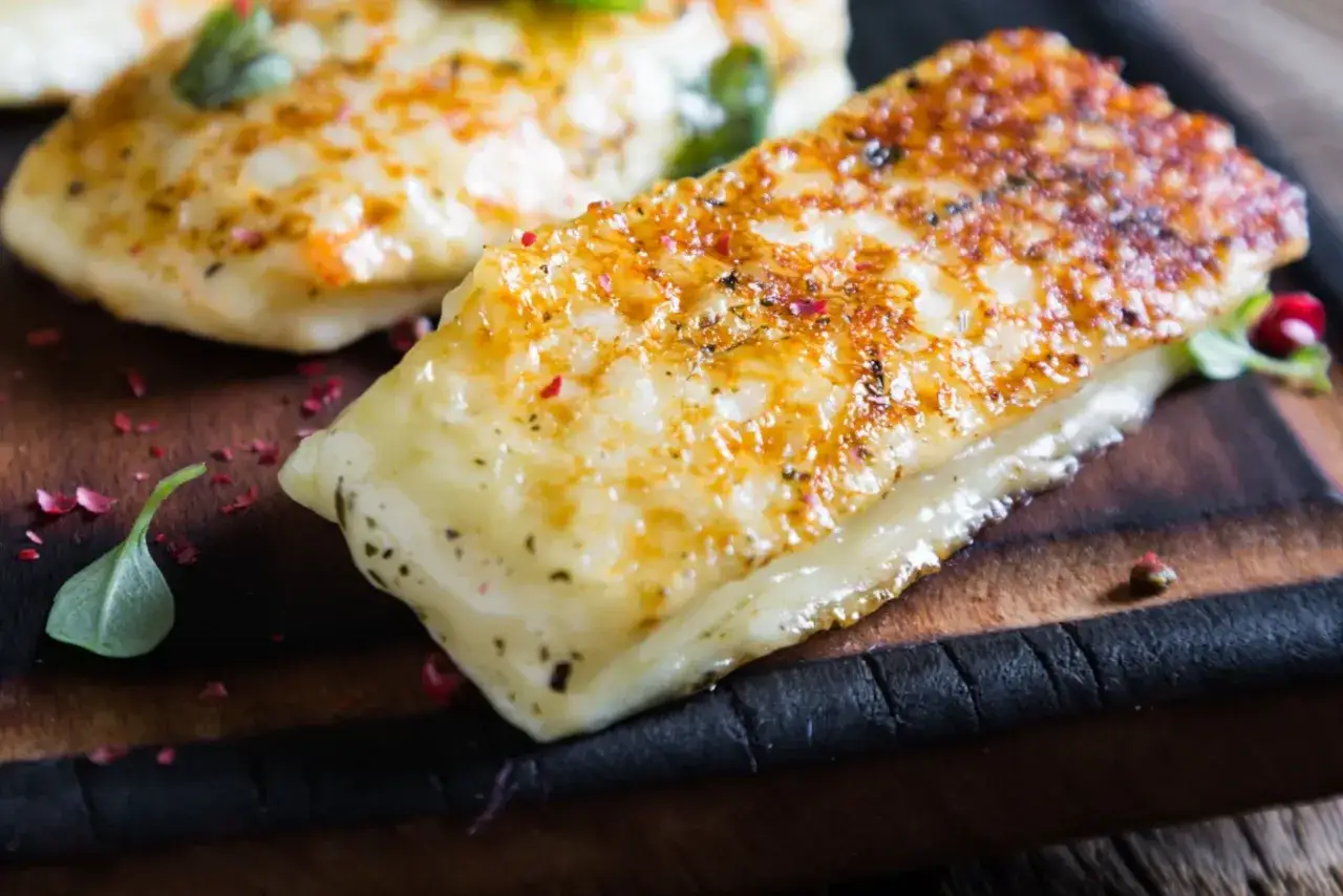 Złociste halloumi z grilla, lekko przypieczone, z ziołami i różowym pieprzem, na drewnianej desce.