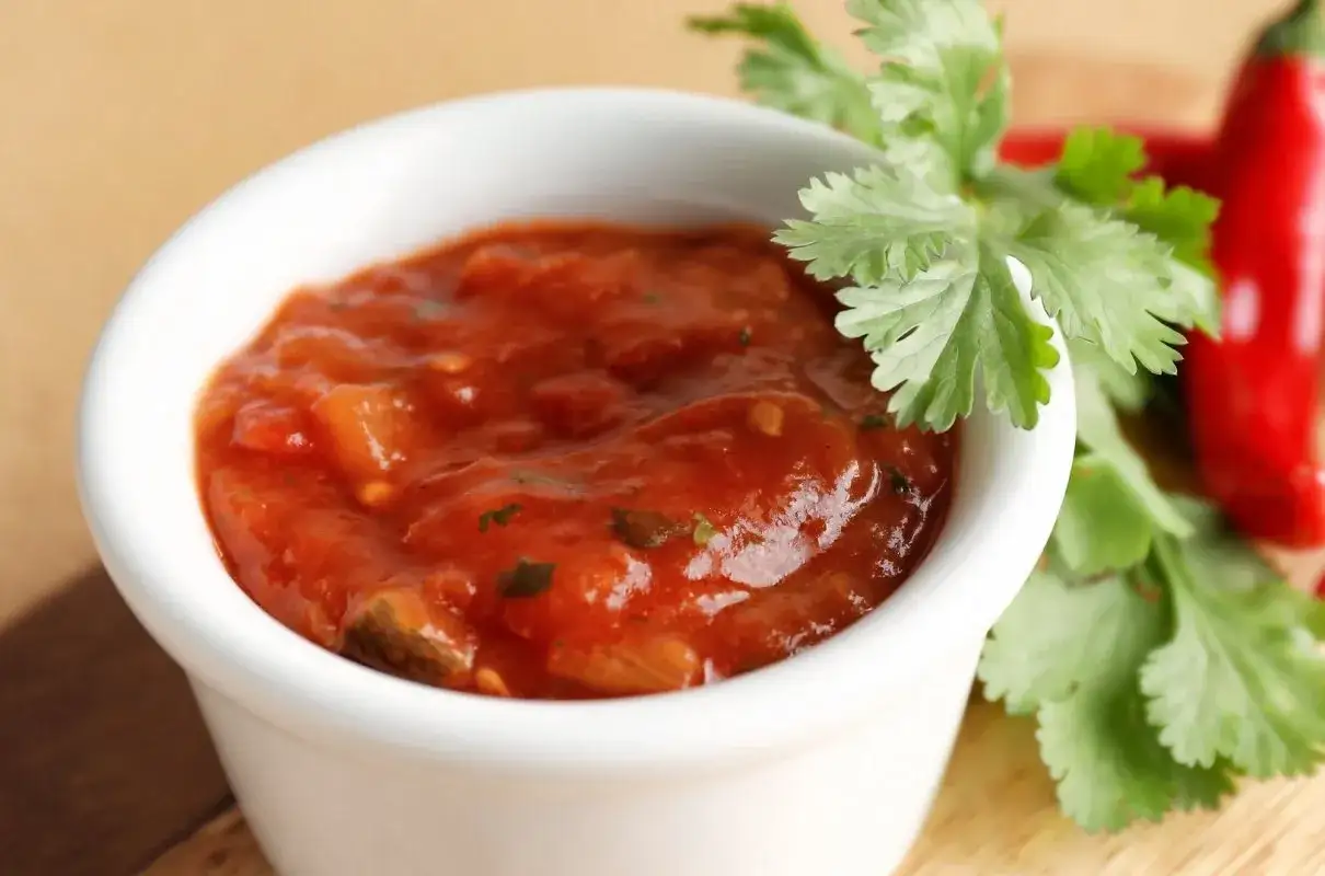 Pikantny sos meksykański w białej miseczce, ozdobiony świeżą kolendrą i papryczkami chili. Idealny dodatek do nachos.