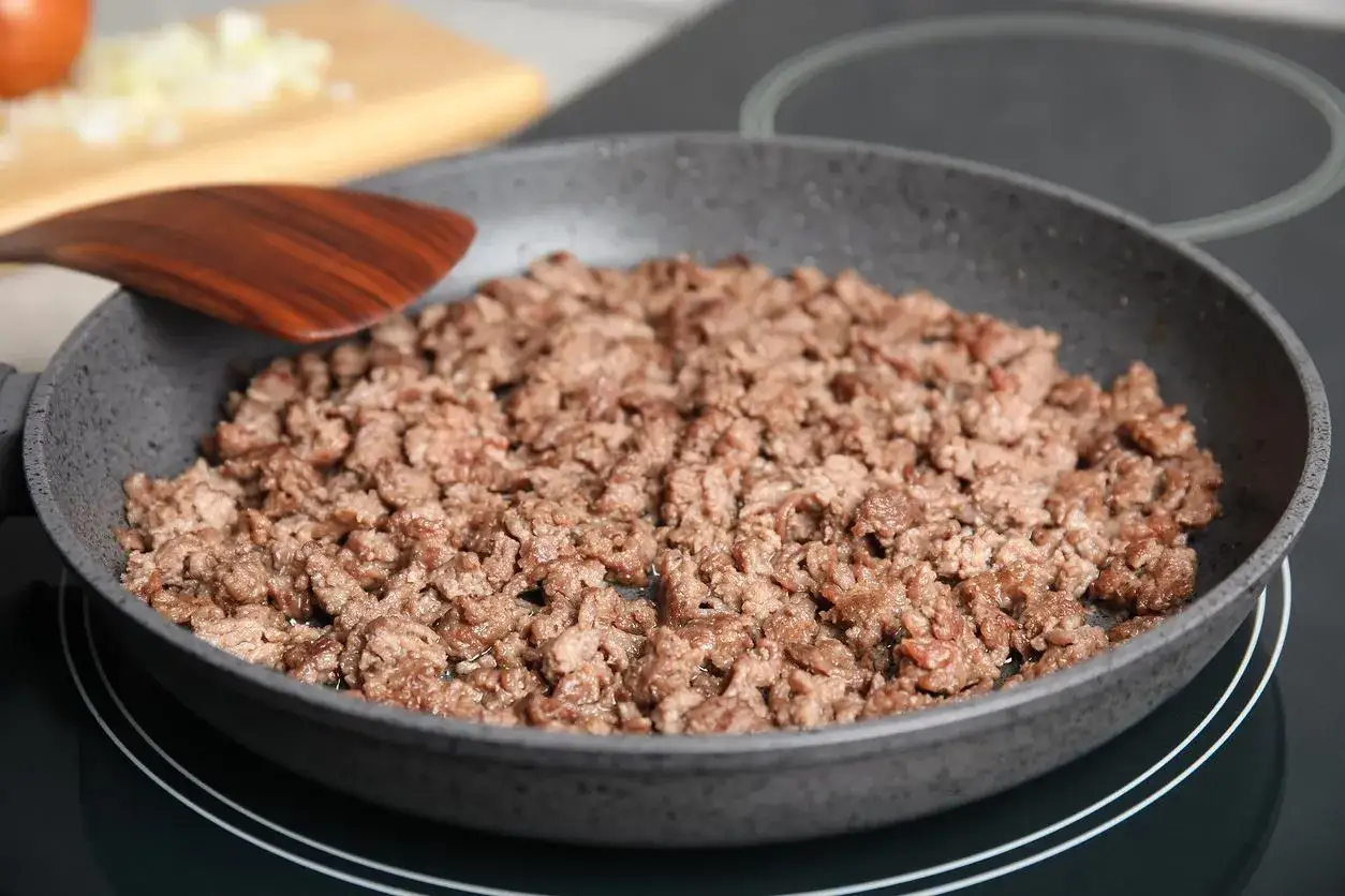 Mięso mielone smaży się na patelni, przygotowując je do spaghetti. W tle widać posiekaną cebulę.
