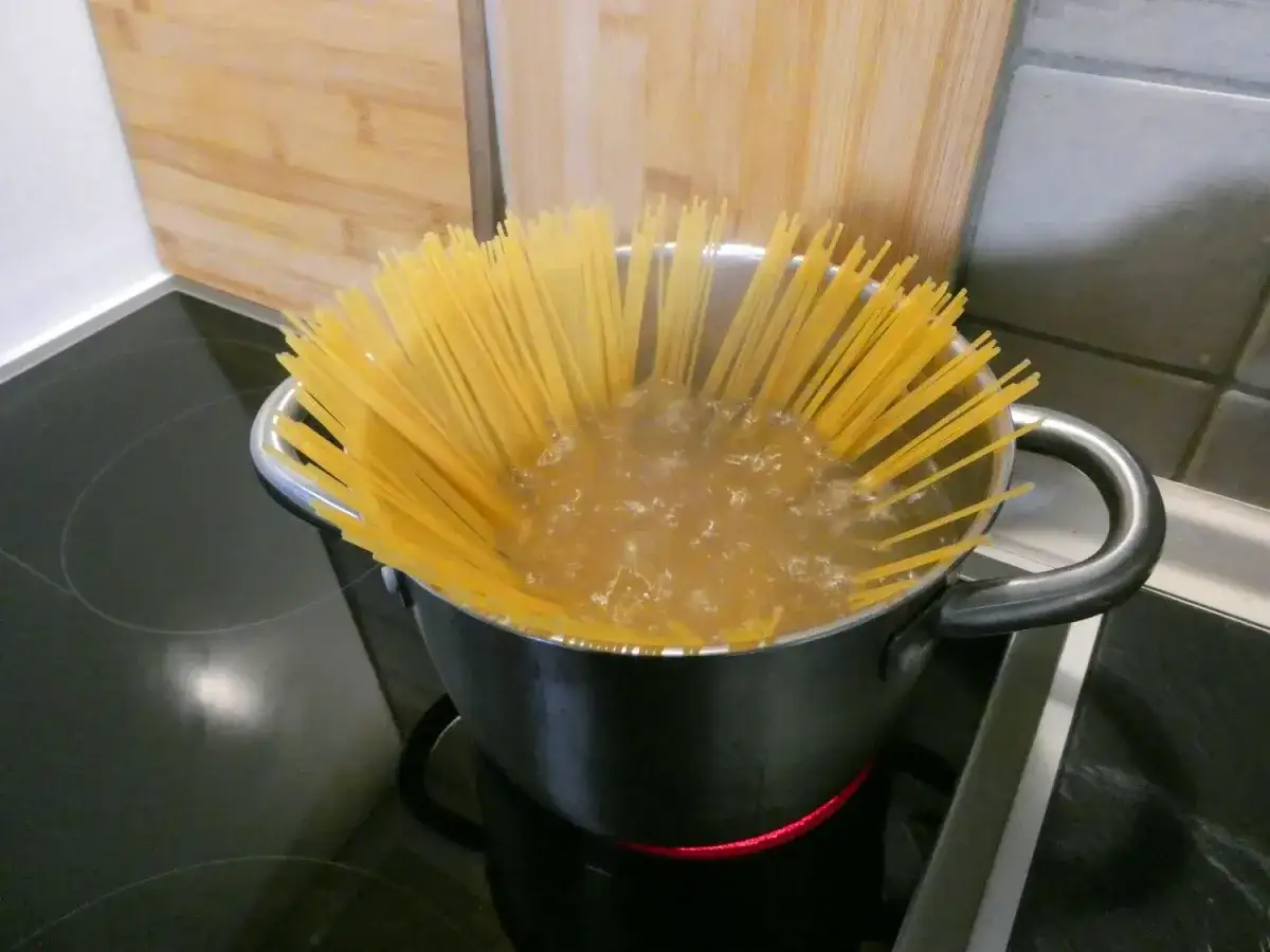 Długi makaron spaghetti powoli zanurza się w bulgoczącej wodzie. Tak właśnie wrzuca się makaron do gotującej wody, by był idealnie al dente.