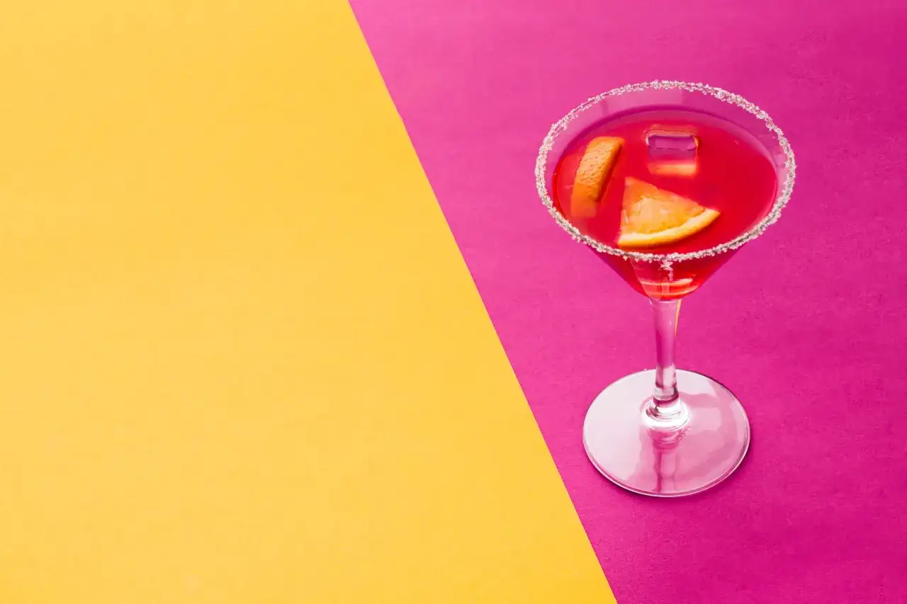 Elegancki cosmopolitan z pomarańczą i lodem, na tle żółto-fuksjowym. Idealny na wieczór w wielkim mieście.